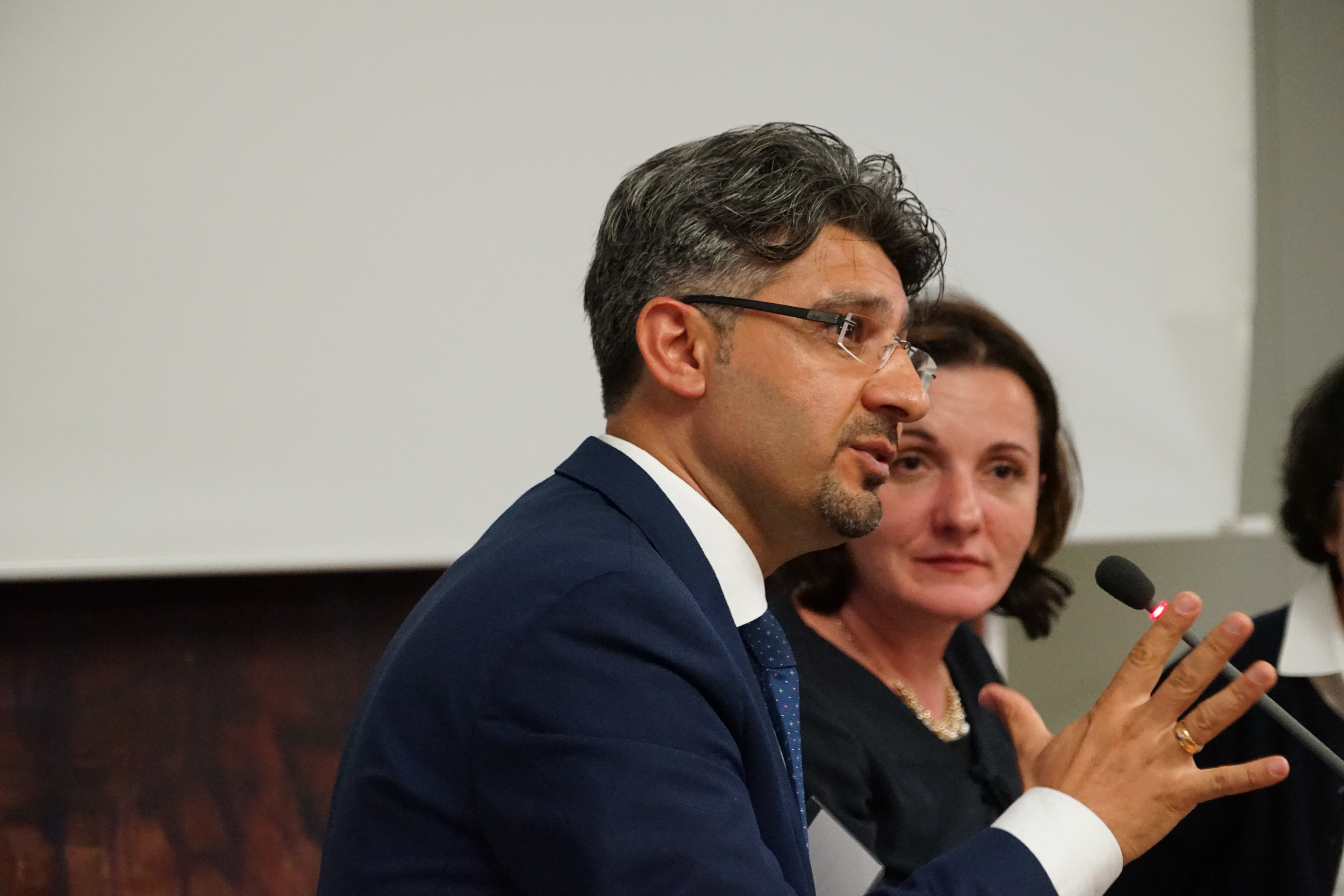 Ein Podiumsteilnehmer spricht gestikulierend ins Mikrofon, neben ihm eine Teilnehmerin