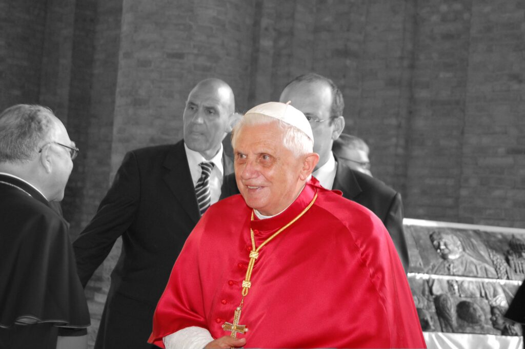 Papst Benedikt XVI. in roter Mozzetta, umgeben von Begleitern