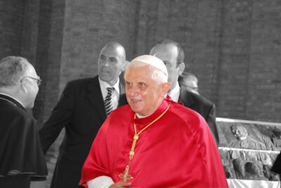 Papst Benedikt XVI. in roter Mozzetta, umgeben von Begleitern