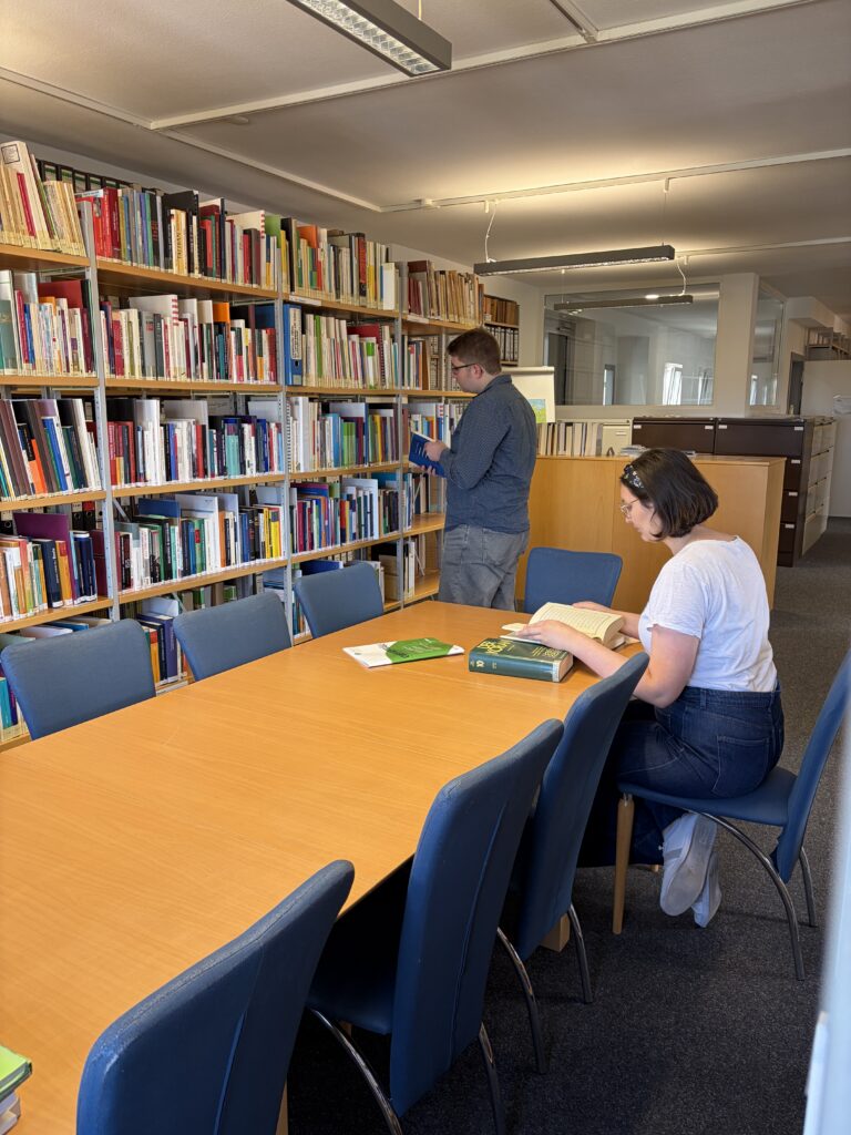 Lesesaal der CIBEDO-Bibliothek: Eine Frau liest am Tisch, ein Mann sucht am Regal